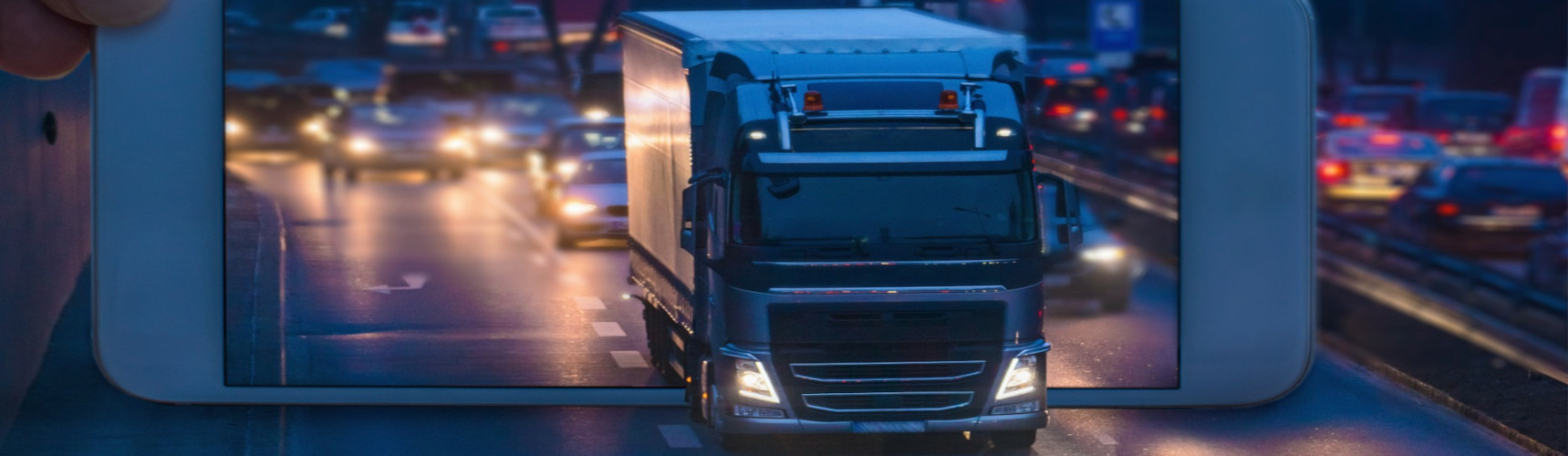Um caminhão sai de um smartphone e adentra uma rodovia em um fundo urbano e a noite.