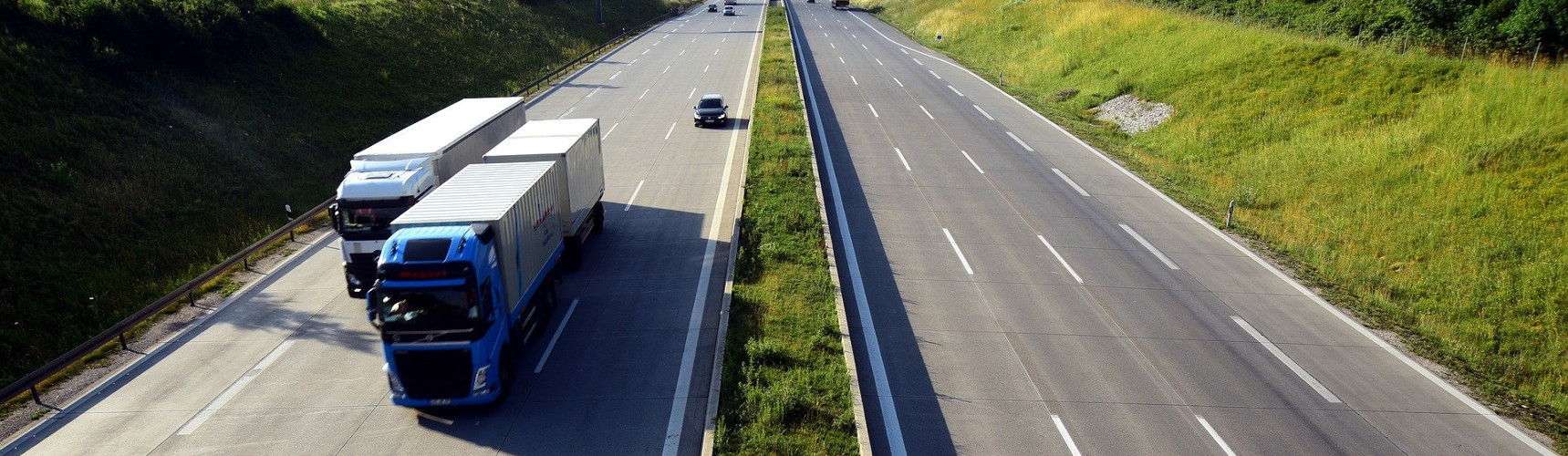 Transporte rodoviário de cargas: em primeiro plano dois veículos pesados transitam com carga na rodovia