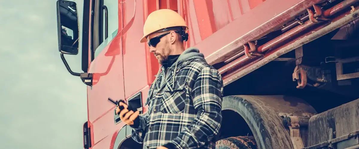 Consulta RCTRC: imagem mostra um motorista ao lado do caminhão verificando informações no celular.